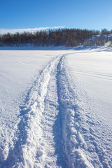 Fototapeta na wymiar Trail from a snowmobile on a frozen and snowy river bed.