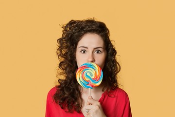 Portrait of a young woman holding lollipop in front of face over colored background