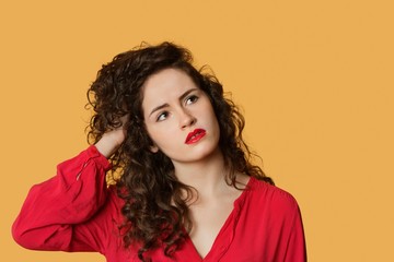 Thoughtful young woman with hand in hair over colored background