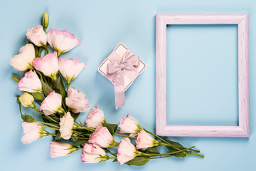 Empty white frame, present box and flowers eustoma on blue paper background with copy space. Flat lay. Love concept