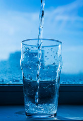 pouring water into glass on blue background
