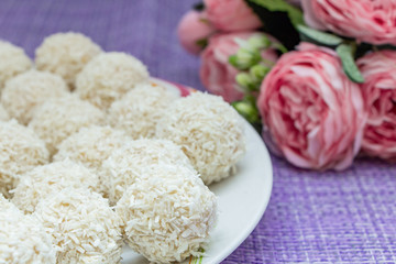 Homemade coconut candy on a background of pink flowers. Sweets for Valentine's Day.