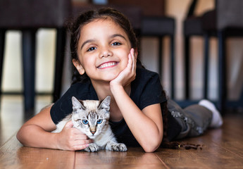Sweet and Happy little girl child with her kitten cat on the floor in the house.  Brunette and brazilian.