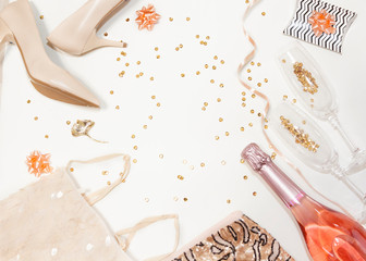 Women accessories party creative composition: shoes, decorations, glasses and bottle of champagne, clothes,  gifts, confetti on white background. Top view, flat lay, copy space