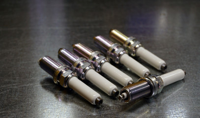 Spark plugs for a modern engine on a steel background. Six spark plugs, one in focus, the rest in the background blurred. Original spare parts for a modern car as a guarantee of quality, durability.