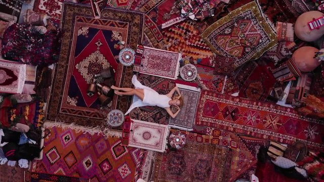  Beautiful happy girl in a long white dress laying on the carpet and rugs in Goreme, Cappadocia, Turkey. Top view drone.