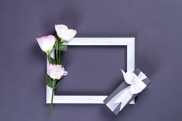Empty white frame, present box and flowers eustoma on dark paper background with copy space. Flat lay. Love concept