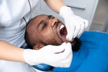 Young african-american man visiting dentist's office for prevention and treatment of the oral cavity. Man and woman doctor while checkup teeth. Healthy lifestyle, healthcare and medicine concept.