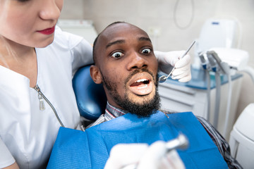 Young african-american man visiting dentist's office for prevention and treatment of the oral cavity. Man and woman doctor while checkup teeth. Healthy lifestyle, healthcare and medicine concept.