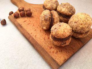 Homemade hazelnut sandwich cookies with chocolate filling on wooden board. Sweet pastry food photograph.