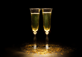 Two glasses of champagne on the golden sequins isolated on a black background. New year greeting card. Text space.