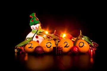 New Year 2020 is coming concept. Numbers written in black ink on the tangerines with xmas decoration, snowman and lights on the black background