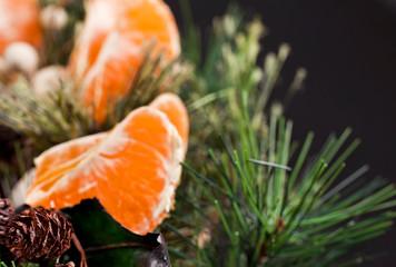 Pine branches and cones with tangerine pieces on a black background. New year greeting card.