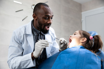 Young caucasian girl visiting dentist's office for prevention and treatment of the oral cavity. Child and african-american doctor while checkup teeth. Healthy lifestyle, healthcare and medicine