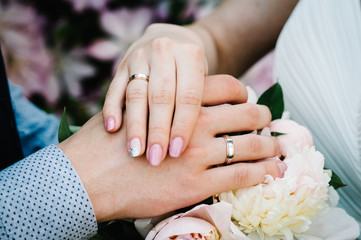 Obraz na płótnie Canvas Hands are newlyweds with wedding rings. Close up On the background of a wedding bouquet of flowers of peonies. Bride Manicure.