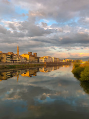 Arno river embankment in Florence, houses and clouds are reflected in the water