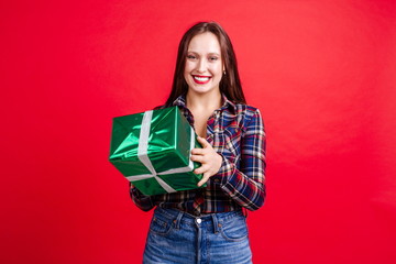 Happy girl in a plaid shirt holding a gift box standing on a red background