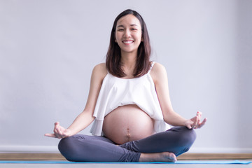 Young pregnant woman practicing yoga while sitting in lotus position at home