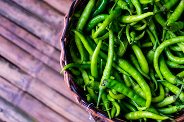 Organic green chili peppers in a rattan basket. This pepper is nutritious with high in antioxidant, contains vitamins and minerals, and helps lose weight. Flay lay. Copy space. Selective focus.