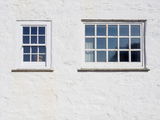 Wide closeup of wooden windows on white plaster walls of a house on a sunny day. Cape Cornwall, United Kingdom. Travel and architecture.