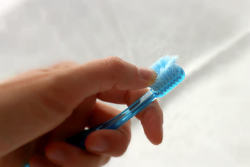 Used old toothbrush with a frayed bristles in hand on light background - obrazy, fototapety, plakaty