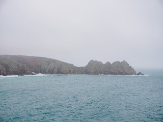 Wide angle view of the distant granite cliff formations making up Porthcurno beach on a foggy day. Cornwall, United Kingdom. Travel and Nature. - 310907370