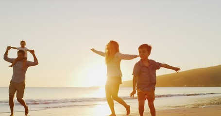 Happy family with young children playing on the beach together, young boys and their parents playing airplane on the beach, amazing family vacation