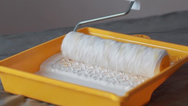 Paint roller rolling in a yellow paint tray with white paint.