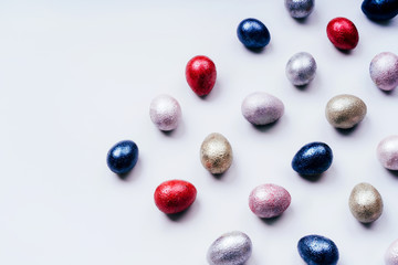 Colored painted pearl chicken and quail eggs of pink, silver, golden and blue color on a light blue pastel background. Minimalistic creative classic easter festive flat lay. Copyspace for text