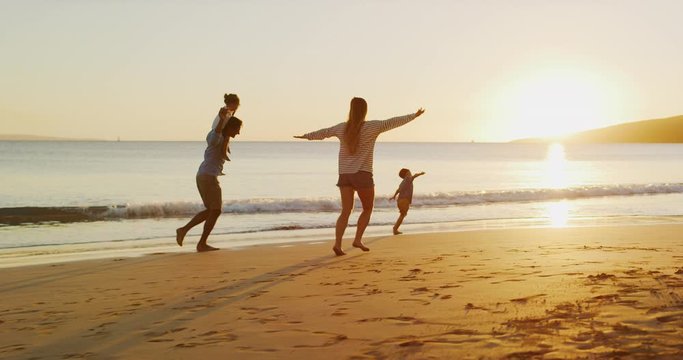 Happy family with young children running and flying into the sunset at the beach, family fun at the beach, joyful parenthood moments