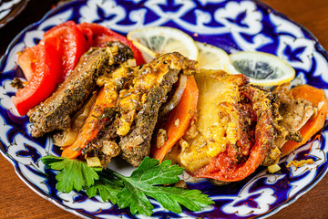Traditional oriental cuisine. Dish for the holiday of Navruz from meat, fish, pineapple, paprika, tomato and lemon. Serving dishes in Uzbek plates. Copy space, background image