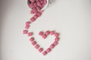 Lots of pink sugar candies on a white wooden background in the shape of a heart
