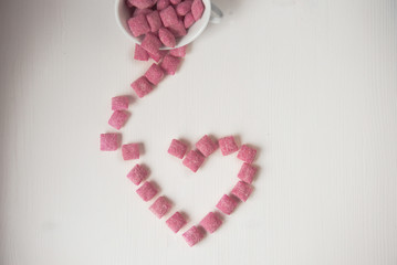 Lots of pink sugar candies on a white wooden background in the shape of a heart