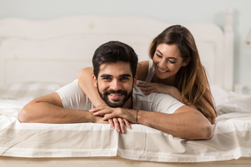 Obraz premium Beautiful couple relaxing together on a bed at home. Man is looking at camera