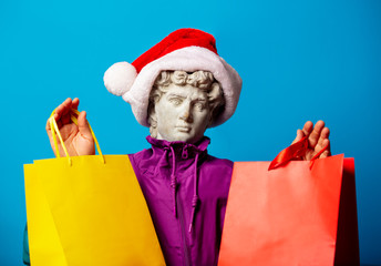 antique statue dressed in trendy clothes of the nineties and Santa Claus hat with shopping bags