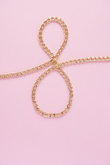 a gold chain laid out in the shape of a eight on a pink background