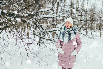 Young attractive blonde in a warm down jacket, knitted mittens, a scarf and a hat in a cold winter forest - warm and cozy clothes