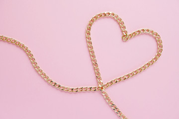 a gold chain laid out in the shape of a heart on a pink background