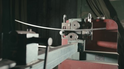 Forge workshop on table. Smithy manual production. Worker bends the metal rod on the wrought iron round bending machine. Manufacturing of a designer part from a metal rod. The blacksmith manufacture.
