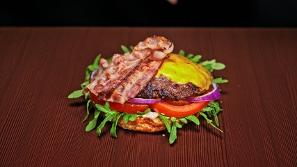 Craft burger is cooking on black background. Consist: sauce, arugula, tomato, red onion, bacon, red currant sauce, ricotta cottage fresh cheese, air bun and marble meat beef. Not made ideal. Looks