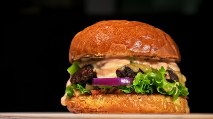 Craft burger is cooking on black background. Consist: red sauce salsa, lettuce, red onion, pickle, cheese, chilli green pepper, air bun and marbled meat beef. Not made ideal. Loving hand made.