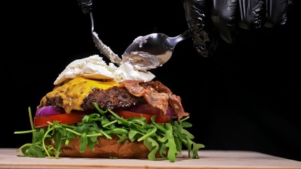 Craft burger is cooking on black background. Consist: sauce, arugula, tomato, red onion, bacon, red...