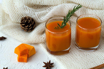 Fresh drink. cocktail with sprig of rosemary with the warm white plaid on white table.glass of fresh pumpkin or oranges juice with slices of pumpkin, spices.