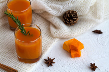 Fresh drink. cocktail with sprig of rosemary with the warm white plaid on white table.glass of fresh pumpkin or oranges juice with slices of pumpkin, spices. top view