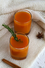 Obraz na płótnie Canvas Fresh drink. two glasses of fresh juice of pumpkin or oranges sprig of rosemary, spices and the warm white plaid on white table. top view