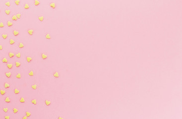  yellow confetti in the shape of hearts on a pink background copy space.