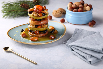 Natural dessert for a Christmas and New Year table made from baked apples with honey, almonds, raisins, hazelnuts, dried apricots, walnuts, on a turquoise plate with sweet, honey-ginger sauce.
