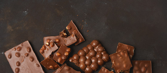 The chunks of broken different chocolate bars with nuts on the black stone surface with space for text. Background with chocolate. Sweet food photo concept.