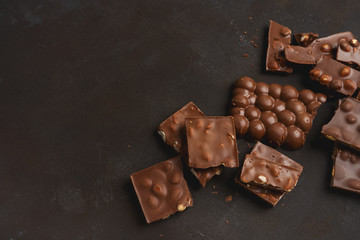 The chunks of broken different chocolate bars with nuts on the black stone surface with space for text. Background with chocolate. Sweet food photo concept.