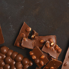 The chunks of broken different chocolate bars with nuts on the black stone surface with space for text. Background with chocolate. Sweet food photo concept.